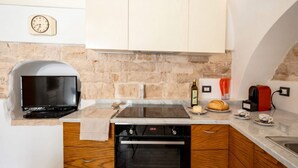 Una cocina con pared de piedra, horno empotrado, televisor de pantalla plana y cafetera.