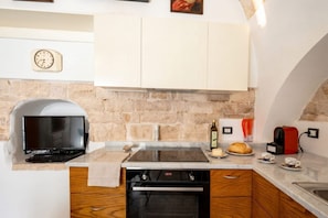 A kitchen with a stone wall, a built-in oven, a flat-screen TV, and a coffee machine. - Dimora BoxFish | Elegance and Relaxation with a Private Terrace (Polignano a Mare)