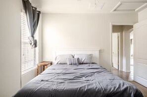 A bedroom with a bed, a bedside table, a window with curtains, and a door leading to another room. - 3-bedroom house in fabulous Tucson with cool AC for relaxing stay (Tucson)