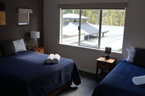 A hotel room with two beds, a window with a view of a building, a lamp on a nightstand, and a basket. - Dual Apartment (10 pax) for Group Bookings, 30 metres from the River (Margaret River)