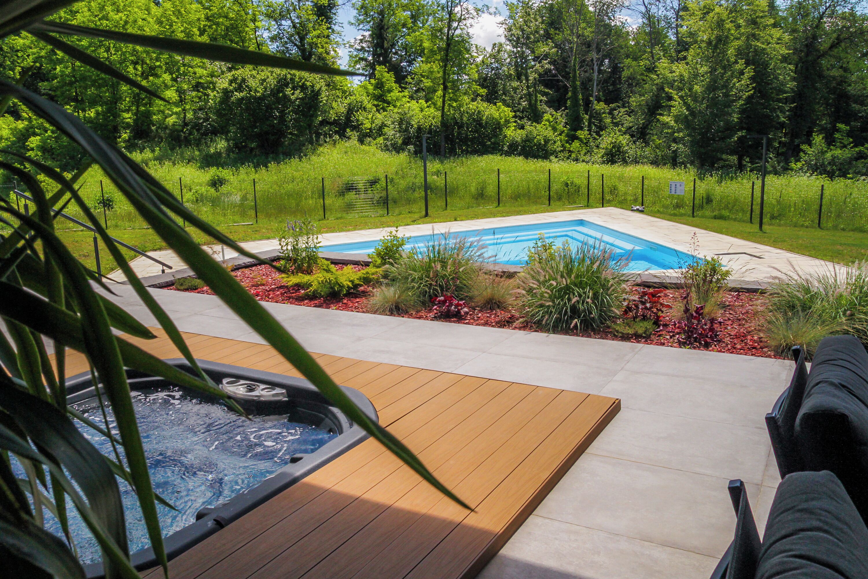 A hot tub on a wooden deck with a pool in the background.
