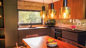 A modern kitchen with a wooden dining table, a fruit bowl, and pendant lighting.