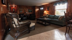 Une pièce aux murs lambrissés, avec un canapé, des fauteuils, une table basse et une lampe.