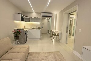 A modern kitchen with white cabinetry, a dining area with a table and chairs, and a living room with a sofa and a small side table. - Spacious Ocean-Front Room Ideal for Relaxation | For Large Family or Groups! (N/A)