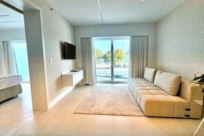 A modern living room with a sofa, a flat-screen TV, and a large sliding glass door leading to a balcony. - Spacious Ocean-Front Room Ideal for Relaxation | For Large Family or Groups! (N/A)