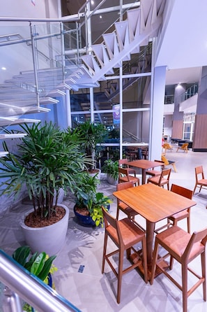 Un espacio interior moderno con una escalera, mesas de madera y plantas en macetas.