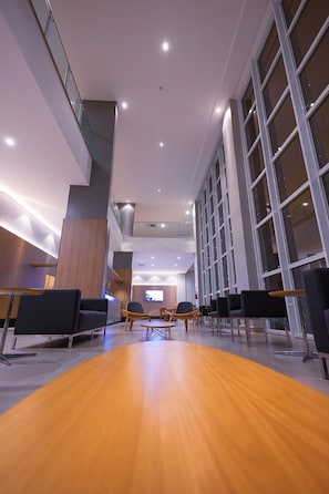 A spacious lobby with a wooden floor, modern seating, and large windows.