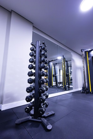 Ein Fitnessstudio mit Hantelgestell, Kraftgeräten und einem Spiegel, der die Geräte reflektiert.