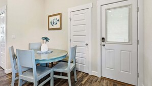 A dining area with a round table, four chairs, a vase with flowers, and two white doors with a window. - SO488 Salvo Sunrise -  Newly renovated oceanside home (Salvo)