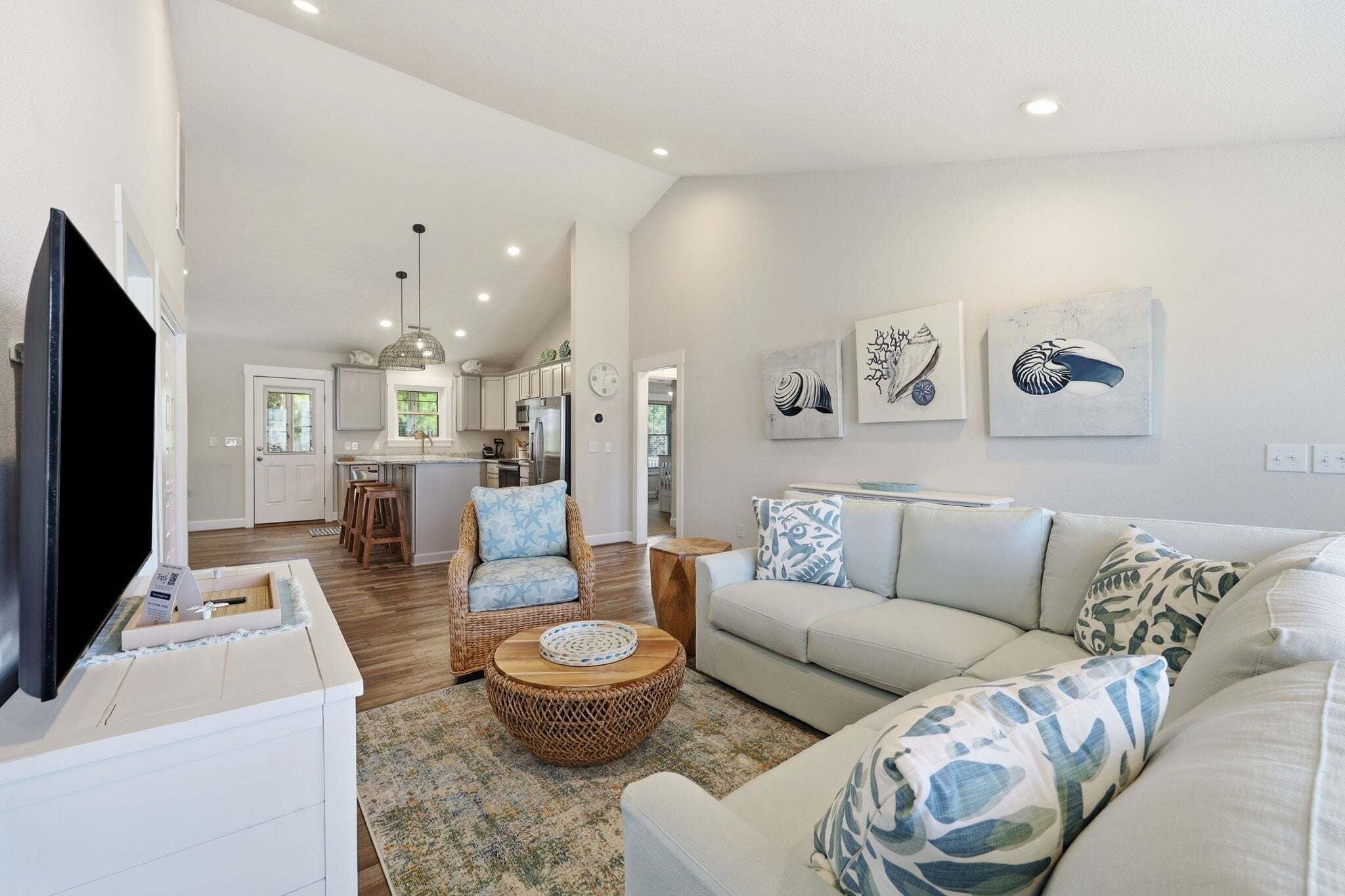 A spacious living room with a large TV, a dining area with a kitchen in the background, and a cozy seating area with patterned cushions.