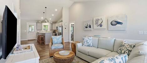 A spacious living room with a large TV, a dining area with a kitchen in the background, and a cozy seating area with patterned cushions.