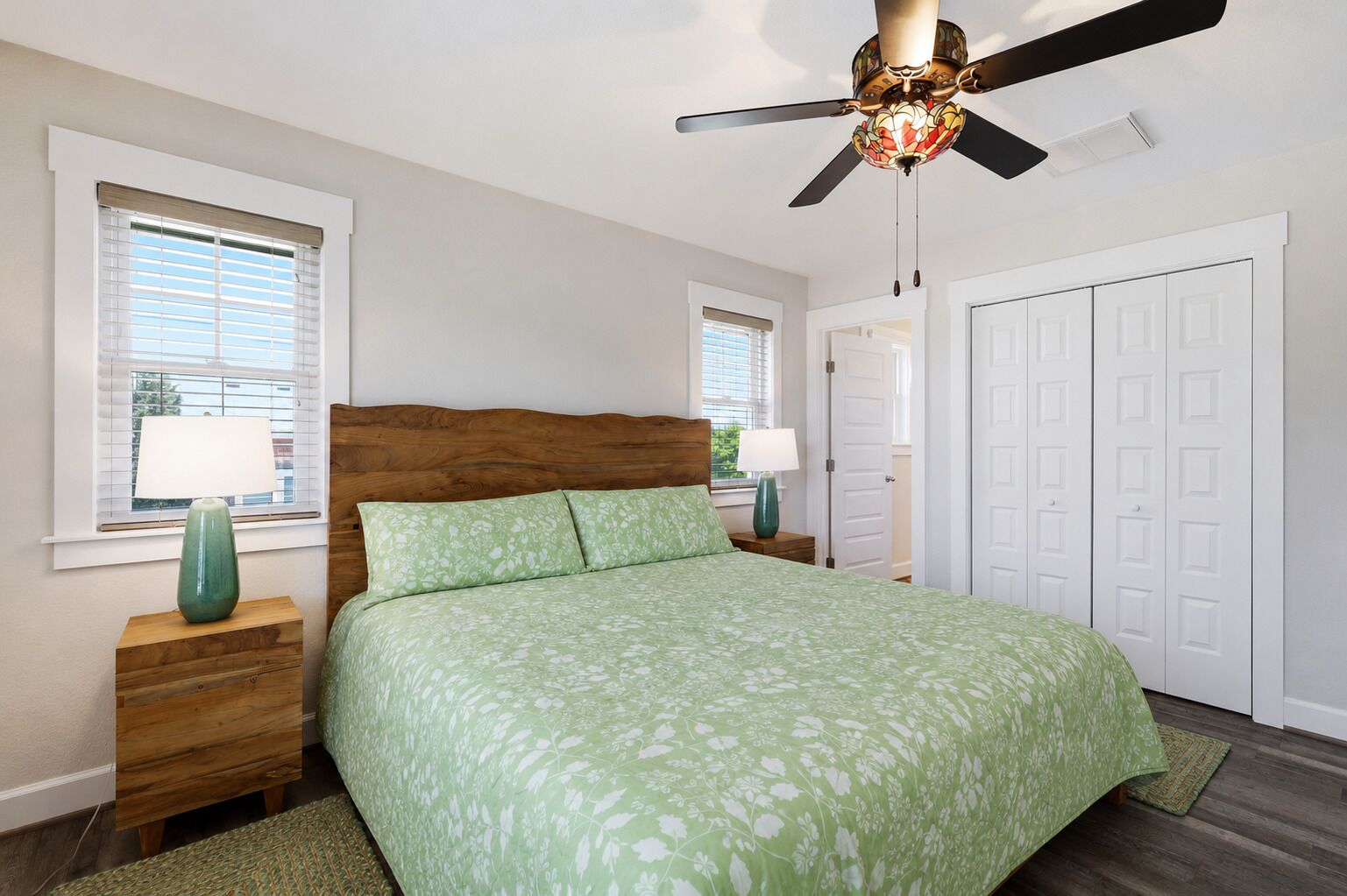 A bedroom with a bed, nightstands, lamps, a ceiling fan, and a wardrobe.