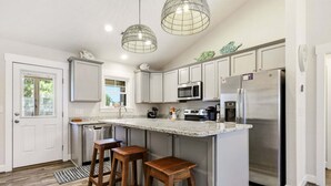 A modern kitchen with white cabinets, stainless steel appliances, a granite countertop, and a bar stool area. - SO488 Salvo Sunrise -  Newly renovated oceanside home (Salvo)