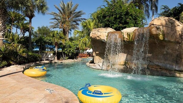 A pool area with clear water, two yellow inflatable tubes, and a waterfall feature. - 7/19-7/24; 3BR/2BA WorldMark Kissimmee Suite. Family Fun, Free Shuttle to Disney (Kissimmee)