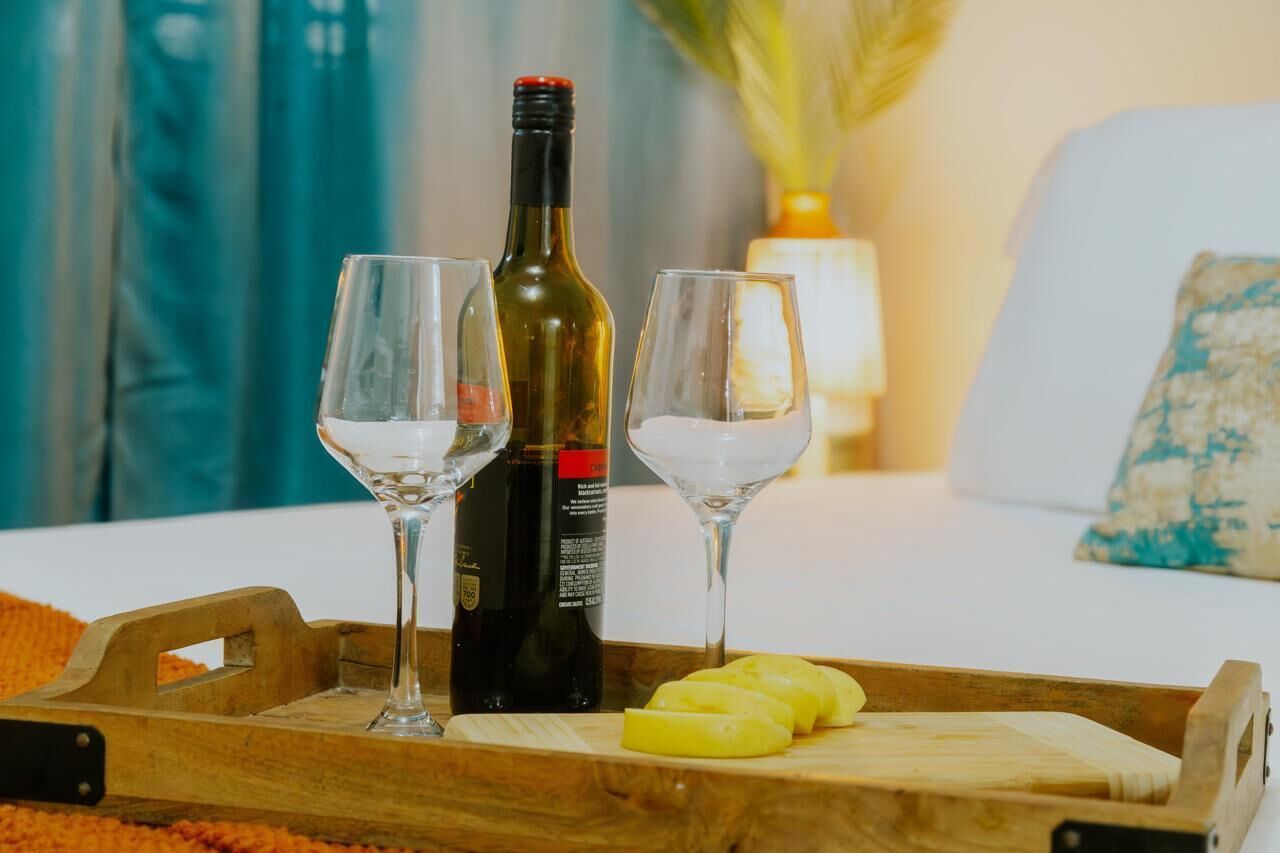 A wooden tray with two wine glasses, a bottle of wine, and pineapple slices on a bed.