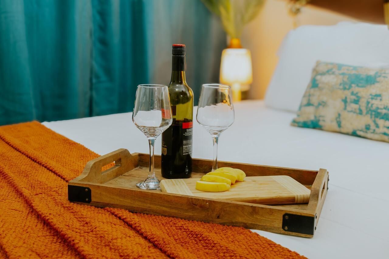 Ein hölzernes Tablett mit einer Flasche und zwei Gläsern auf einem Bett mit einer orangefarbenen Decke.