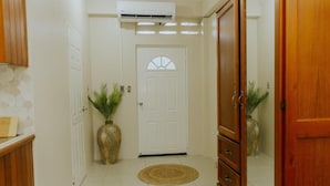 A hallway with a white door, a wooden cabinet, a large woven vase, and an air conditioning unit.
