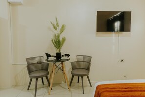 A small room with a bed, a TV mounted on the wall, a table with chairs, and a potted plant.