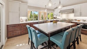 A modern kitchen with a large island, white cabinets, and blue chairs. - Spacious 4BR Estate, Pickleball/Bball Court Surrounded by Trees on 0.74 acres (Poway)