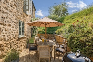 Ein Steinhaus mit einer Terrasse, die einen runden Tisch, Stühle und einen Grill zeigt.