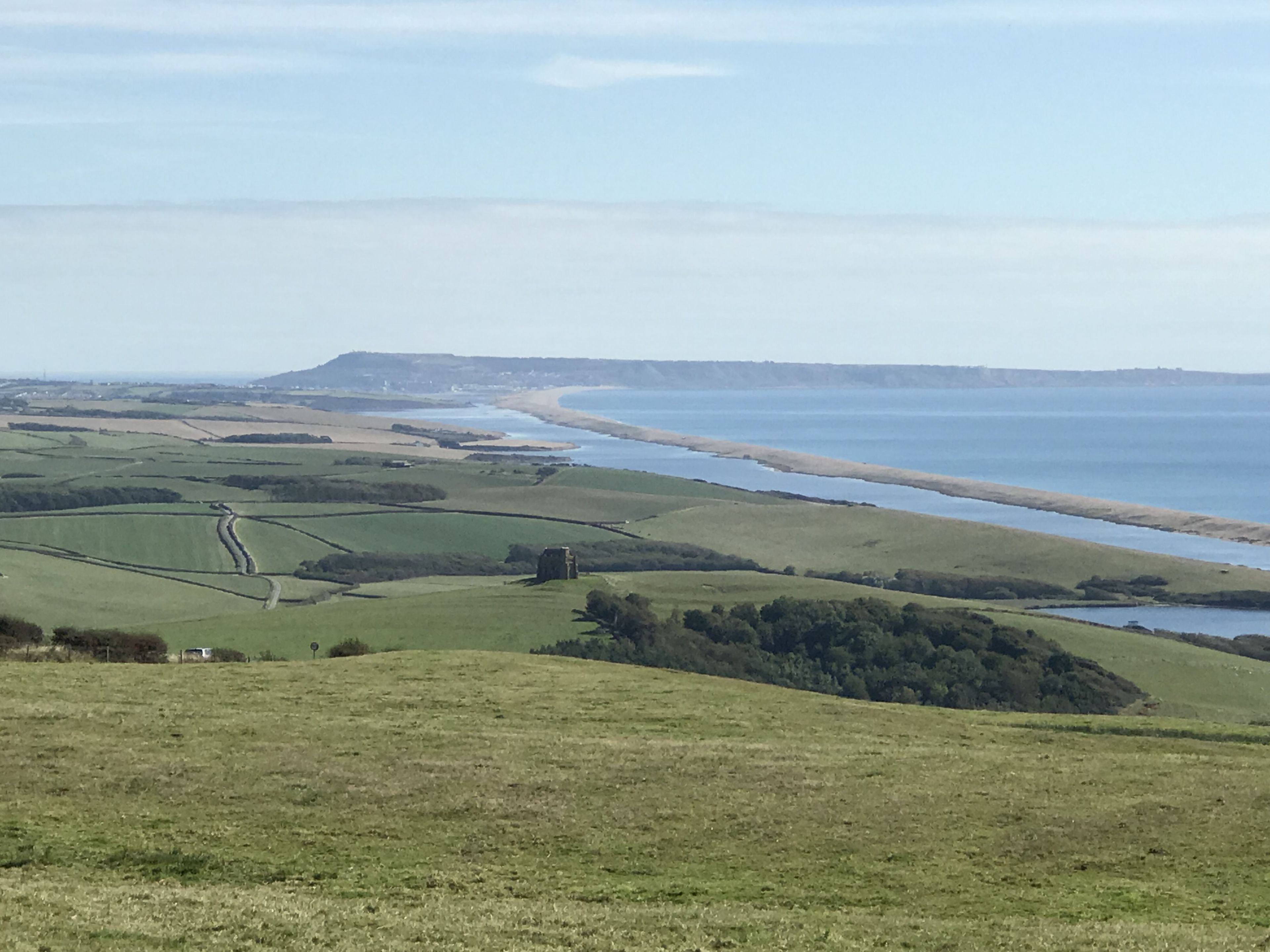 Un paysage côtier avec des champs verdoyants vallonnés, une construction en pierre et une plage.