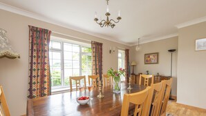 A dining room with a wooden table, chairs, and a chandelier. There are windows with curtains, a vase with flowers, and a painting on the wall. - Greygles (Sleeps 5) -Melcombe Bingham, Dorchester sleeps 5 guests  in 3 bedrooms (Melcombe Bingham)