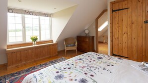 A bedroom with a large window, a bed with a floral bedspread, a wooden dresser, and a chair. - Greygles (Sleeps 5) -Melcombe Bingham, Dorchester sleeps 5 guests  in 3 bedrooms (Melcombe Bingham)