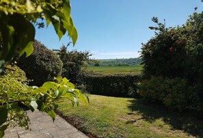 Ein Garten mit befestigtem Weg, üppigem Grün und Blick auf ein entferntes Feld.