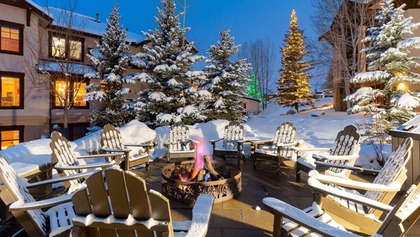 Zona salotto esterna innevata con poltrone in stile Adirondack e un braciere.