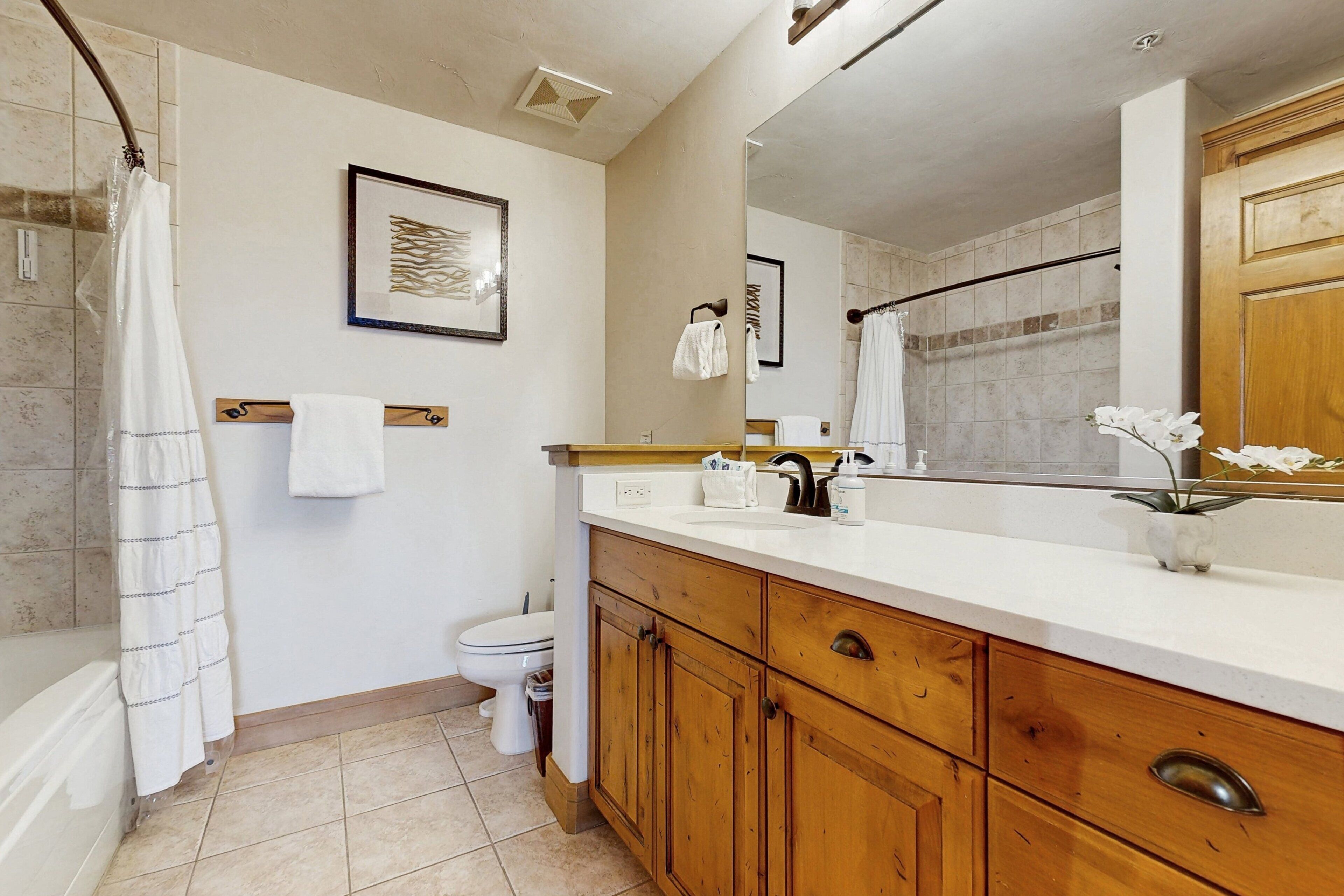 A bathroom with a shower, toilet, wooden vanity, and a large mirror.