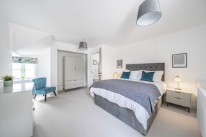 Ein modernes Schlafzimmer mit einem großen Bett, Nachttischen, einem Sessel und einem Fenster mit Blick.