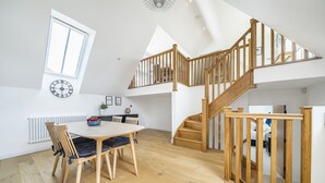Une pièce spacieuse avec un escalier en bois, un coin repas comprenant une table et des chaises, et une grande fenêtre.