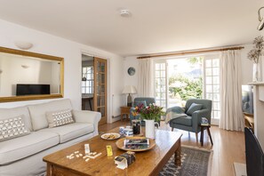 Ein modernes Wohnzimmer mit einer Couch, einem Couchtisch und zwei Sesseln. Es gibt einen Fernseher, eine Lampe und ein Fenster mit Vorhängen.
