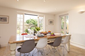 A bright kitchen with a wooden table, three chairs, and a view of the garden through large windows. - The White House (Sleeps 4) -West Lulworth, Lulworth Cove,sleeps 4 guests  in 2 bedrooms (West Lulworth)