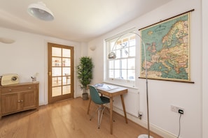 Ein Zimmer mit einem Holztisch, einem Stuhl, einer Karte an der Wand, einer Pflanze und einem Schrank.