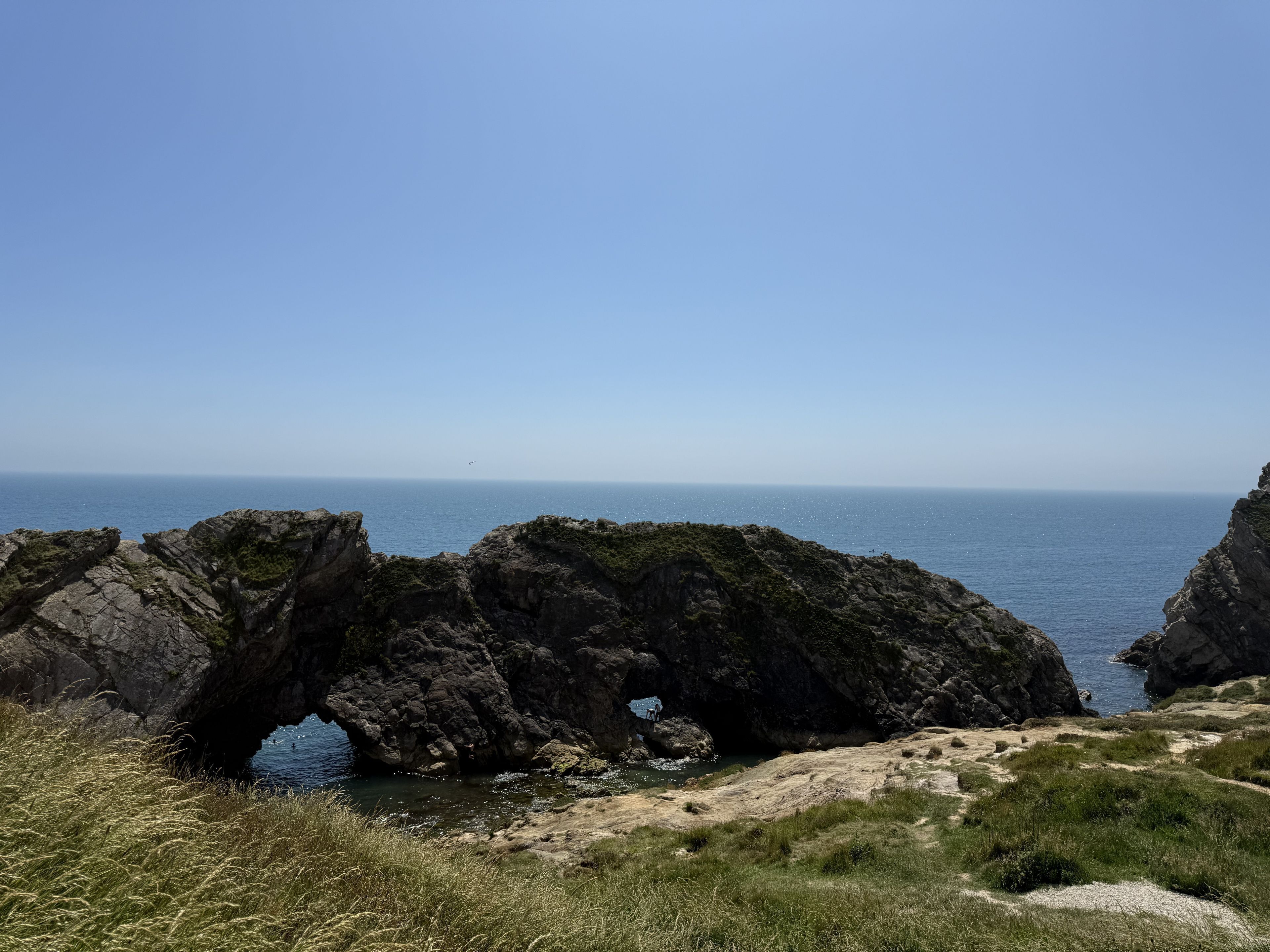 A coastal landscape with rocky formations and a clear sky.