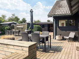 Un patio exterior con mobiliario de madera, una parrilla y una zona de estar cubierta.