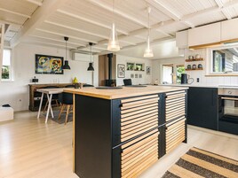 Una cocina moderna con una isla central, iluminación colgante y un comedor con mesa y sillas.