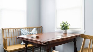 A wooden dining table with a bench, a potted plant, and a window with blinds. - Cute Beach Cottage - Easy walk to Beach, Bay, More (San Diego)