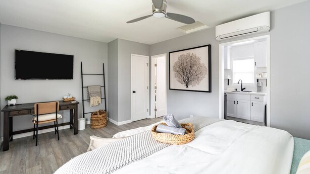 A bedroom with a bed, a desk, a chair, a ceiling fan, a wall-mounted TV, a framed picture, and a kitchenette. - Cute Beach Cottage - Easy walk to Beach, Bay, More (San Diego)