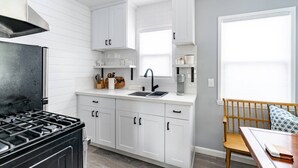 A modern kitchen with white cabinetry, a gas stove, a sink, and a window. - Cute Beach Cottage - Easy walk to Beach, Bay, More (San Diego)