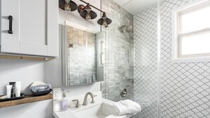 A modern bathroom with a white sink, a mirror, a shower, and a patterned wall. - Cute Beach Cottage - Easy walk to Beach, Bay, More (San Diego)