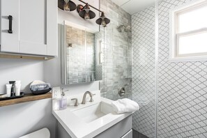 Ein modernes Badezimmer mit einem weißen Waschbecken, einem Spiegel, einer Dusche und einer Wand mit Muster.