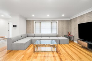 Ein modernes Wohnzimmer mit einem Ecksofa, einem Glastisch, einem Flachbildfernseher und Holzböden.