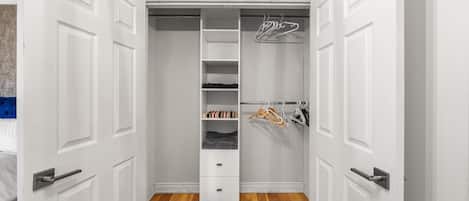 Un vestidor con puertas blancas, suelo de madera y una barra para colgar ropa.