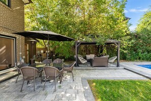 Eine Terrasse mit Gartenmöbeln, einer Pergola und einem Swimmingpool.