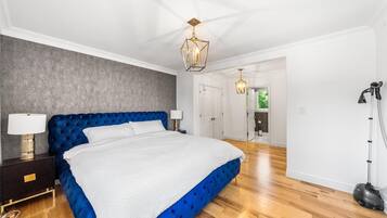 A bedroom with a large bed, a nightstand, a lamp, a ceiling light fixture, and a vacuum cleaner.