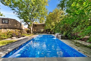 Ein rechteckiger Pool mit Wasserfall, umgeben von einer Holzterrasse und Liegestühlen.