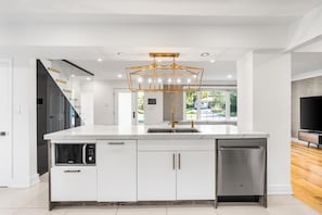 A modern kitchen with a central island, stainless steel appliances, and a unique geometric pendant light.
