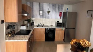 Een kleine keuken met houten kastjes, een vaatwasser, een magnetron en een koelkast.